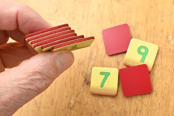 Edge view of six digit cards held in the fingers of one hand. The remaining four cards from a set of ten digits, are lying on the table below.