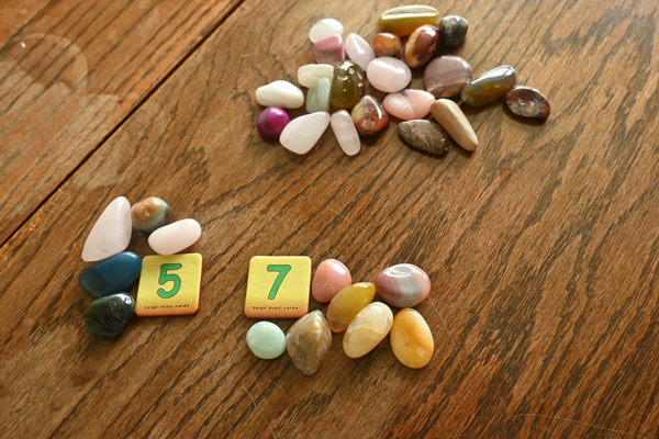 Several piles of smooth coloured stones. Two piles have a card denoting how many stones are in the pile.